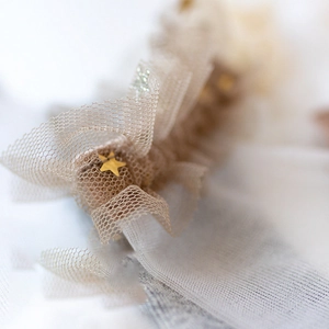 Sheer lace hair accessory with gold star sequins and ruffled beige mesh detail
