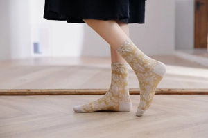 Detail of ginger yellow mid-calf socks with white floral jacquard on wooden floor