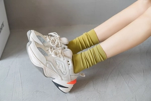 Detail of off-white chunky sneakers with yellow ribbed crew socks on a concrete floor