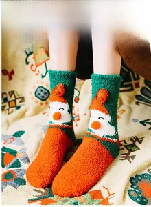 Detail of coral fleece Christmas socks featuring 3D Santa patterns and festive pompoms