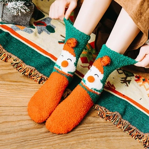 Christmas coral fleece socks with Santa Claus pattern and plush balls on wooden floor