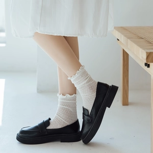 Close-up of white lace crew socks with ruffle edges paired with black matte loafers