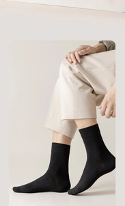 Close-up of black cotton crew socks with ribbed cuffs shown on a male model sitting