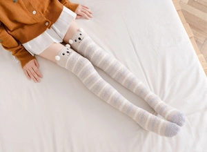 Close-up of over-the-knee coral fleece socks featuring blue stripes and a cute bear face