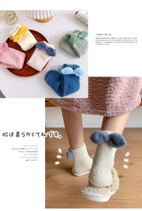 Detail of plush coral fleece socks with 3D bow accent on warm wooden floor background