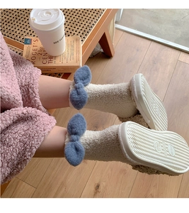 Detailed view of plush coral fleece slippers with blue bow and non-slip textured sole