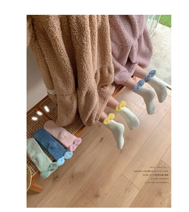 Detail of coral fleece winter socks with plush bows on light wood home background