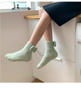 Detail of light green coral fleece socks with back bow tie on model's feet
