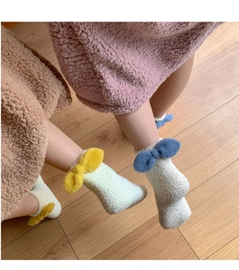 Detail of coral fleece socks with plush bow on wooden floor for winter warmth