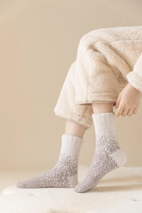 Detail von weichen Socken aus Korallenvlies in Lila und Creme auf weißem Teppich