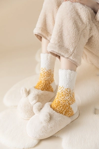 Detailansicht kuscheliger Korallenvlies-Socken und Plüschhausschuhe auf weißem Teppich