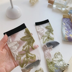 Detail van transparante damessokken met roze en groene bloemmotieven en zwarte boord