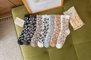 Row of seven colorful leopard print coral fleece winter socks on a green velvet surface