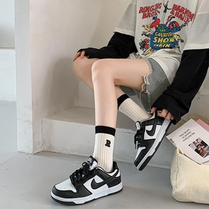 Detail of white cotton crew socks with R embroidery paired with black and white sneakers