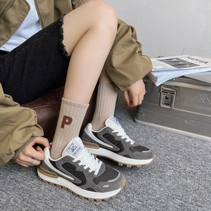 Détail de chaussettes mi-hautes kaki avec broderie P portées avec des baskets rétro