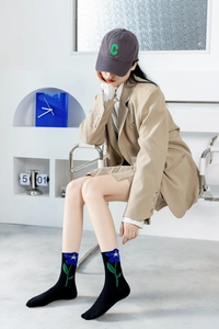 Detailed shot of black crew socks with blue floral embroidery worn with stylish karki blazer