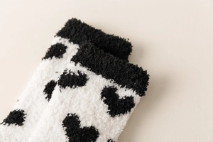 Close-up of fluffy coral fleece socks in white with black heart patterns for winter