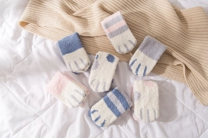 Detail of soft coral fleece cat paw socks in various colors on a cozy home bed background