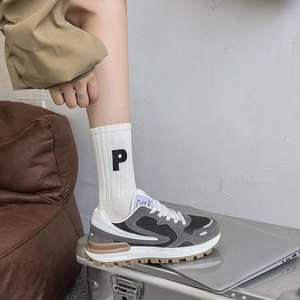 Détail de chaussettes blanches côtelées avec broderie P noire et baskets rétro grises