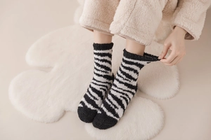 Detail of warm black and white zebra striped coral fleece socks worn on soft carpet