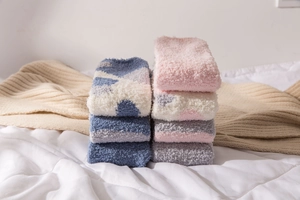 Close-up of thick coral fleece winter socks in multiple colors stacked on a cozy bed