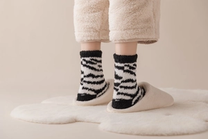 Close-up of warm zebra striped coral fleece socks worn with plush slippers for home comfort