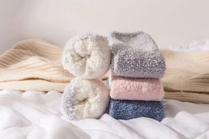 Close-up of thick blue and grey coral fleece socks on a cozy white cotton bed