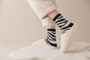 Close-up of zebra stripe coral fleece socks with warm cream home slippers on white rug