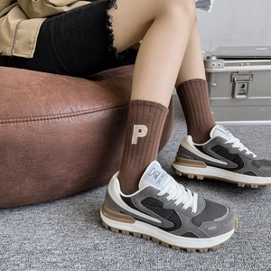 Détail de chaussettes en maille marron avec broderie P et baskets en patchwork mixte