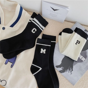 Flat lay of embroidered letter socks in black and cream with striped varsity jacket detail