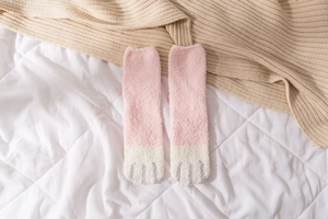 Detail of pink and white coral fleece cat paw socks on a soft quilted surface