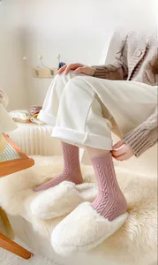 Detail of pink cable knit wool socks paired with plush slippers in a cozy home setting