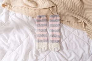 Detail of soft coral fleece striped socks with cute cat paw design on a cozy bed