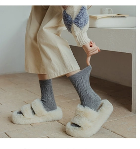 Close-up of grey cable knit wool socks paired with fluffy white slippers for winter warmth
