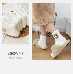 Detail view of white coral fleece socks featuring a cute plush brown bear decoration