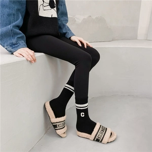 Detailed view of beige plush slippers with black embroidered strap and striped sports socks