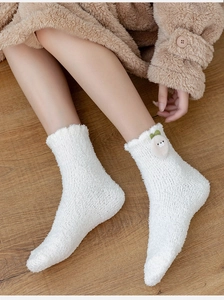 Close-up of thick white coral fleece socks with cute plush animal charm on wooden floor