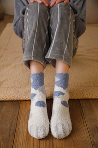 Close-up of fluffy blue and white cat paw coral fleece socks on a warm rug
