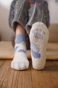 Close-up of soft coral fleece socks with cute blue cat paw prints on a wooden floor