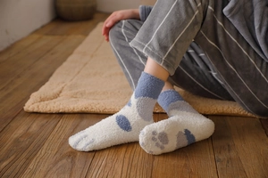 Close-up of cozy blue coral fleece cat paw socks on a soft plush rug and wooden floor
