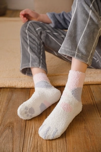Close-up of soft coral fleece socks with blue cat paw design on a cozy carpet