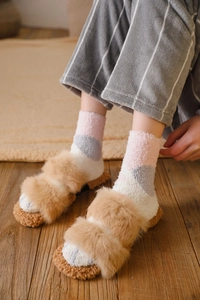 Close-up of fluffy brown slippers and warm coral fleece socks on a wooden floor