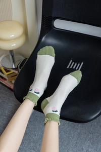 Detail of white cotton socks with avocado green accents and cherry patterns on an ankle cuff