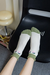 Detail of white cotton socks with green ruffled cuffs and floral embroidery