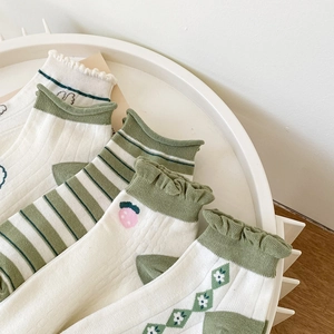 Detail of green and white cotton socks with embroidery and lace trim on a white tray