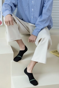 Detail of low-cut black cotton boat socks with green stripes for men on white stairs