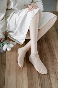 Detail view of sheer beige lace ankle socks with floral embroidery on wooden floor