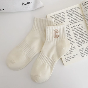 Detailed view of cream cotton knit crew socks with khaki embroidered C letter and ribbed texture