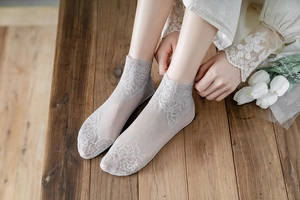 Detail of light gray lace socks with vintage rose floral embroidery on wooden floor
