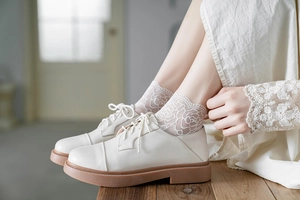 Close-up of white lace socks with floral patterns paired with vintage white leather shoes